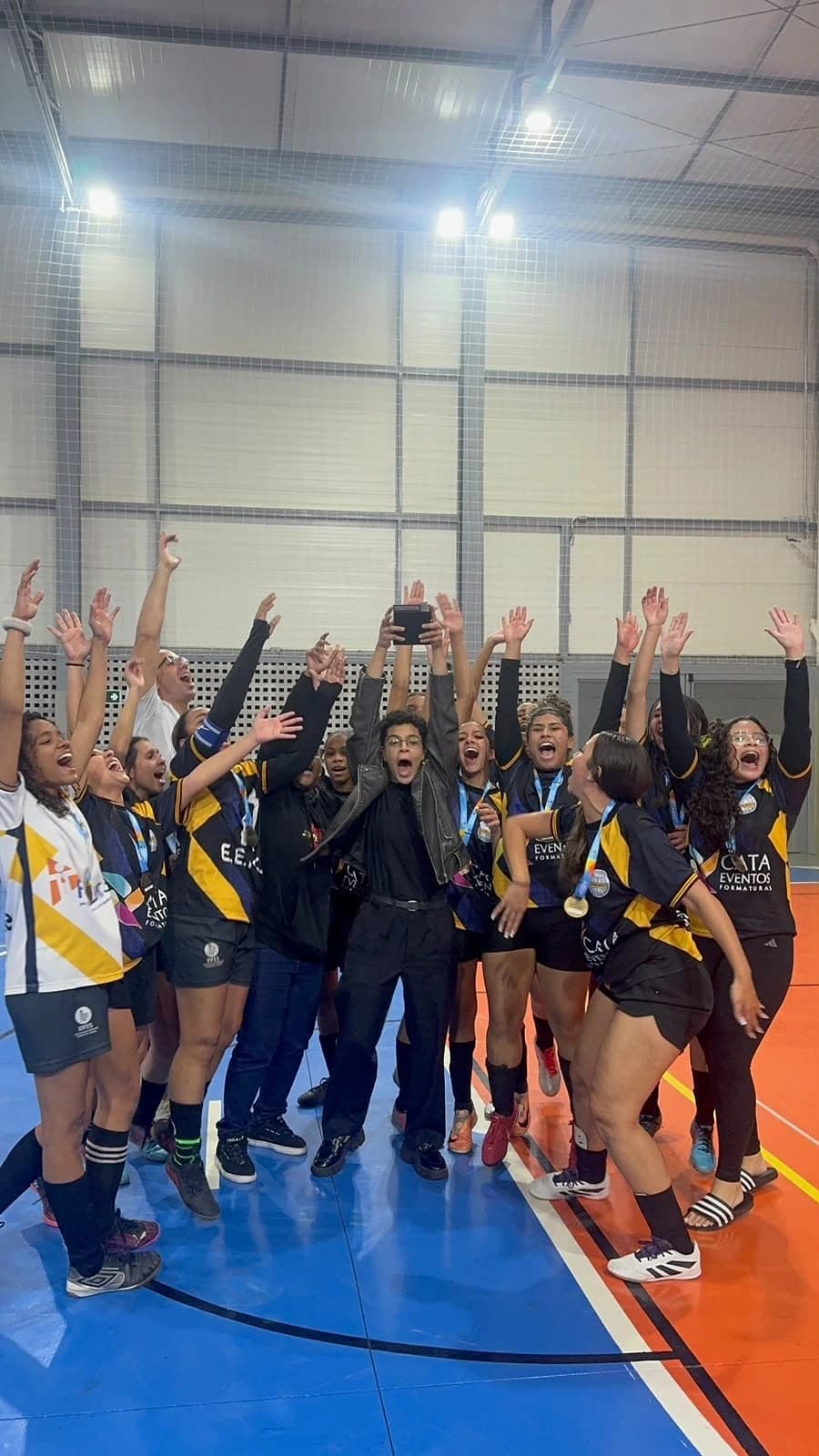 Atletas do Futsal feminino comemorando com as medalhas e o troféu erguido