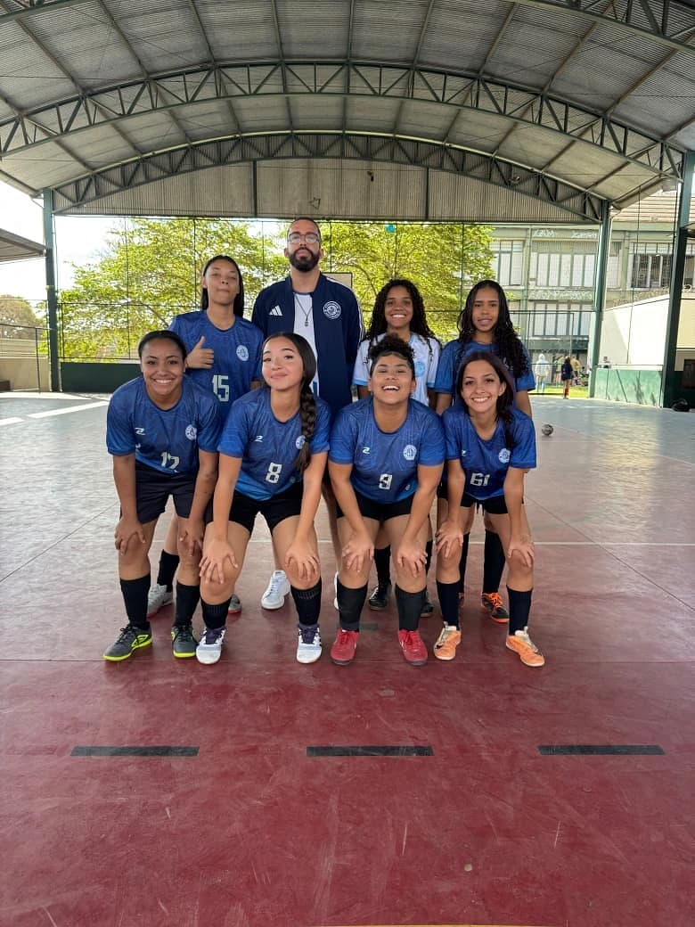 Equipe de Futsal feminino posada com o técnico na quadra coberta