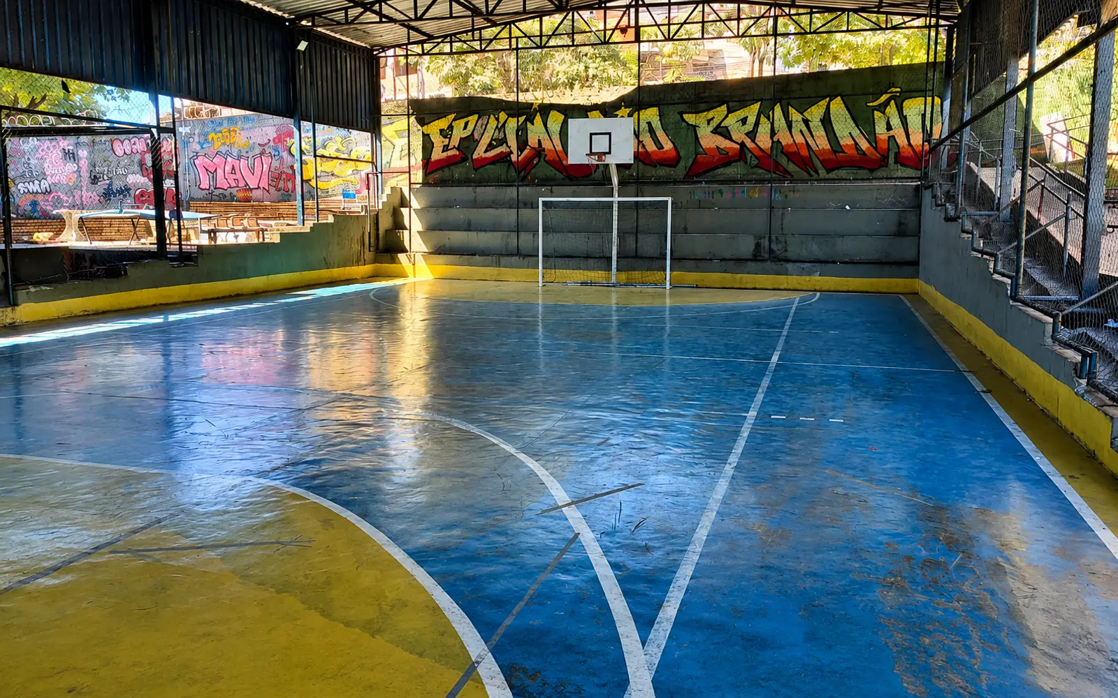 Quadra coberta da Escola Estadual Professor Cláudio Brandão, com o nome da escola grafitado ao fundo