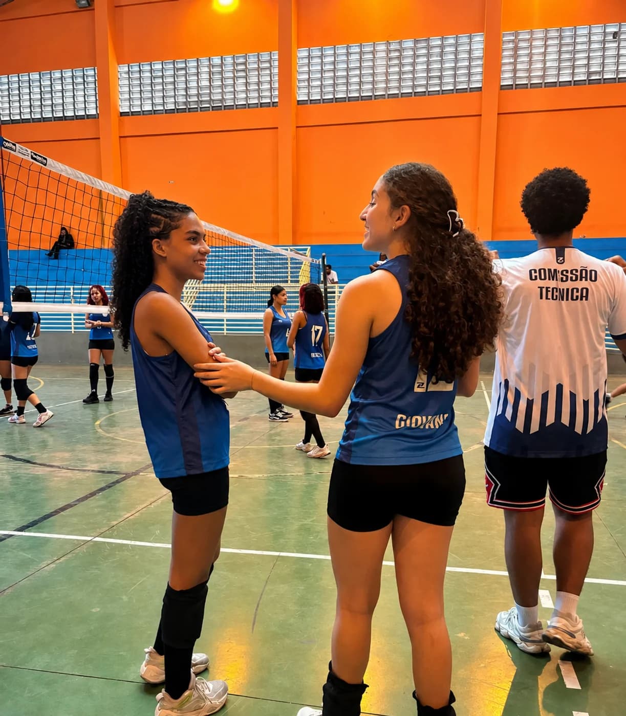 Duas atletas do Vôlei conversando na quadra, ao lado da rede, durante o treino
