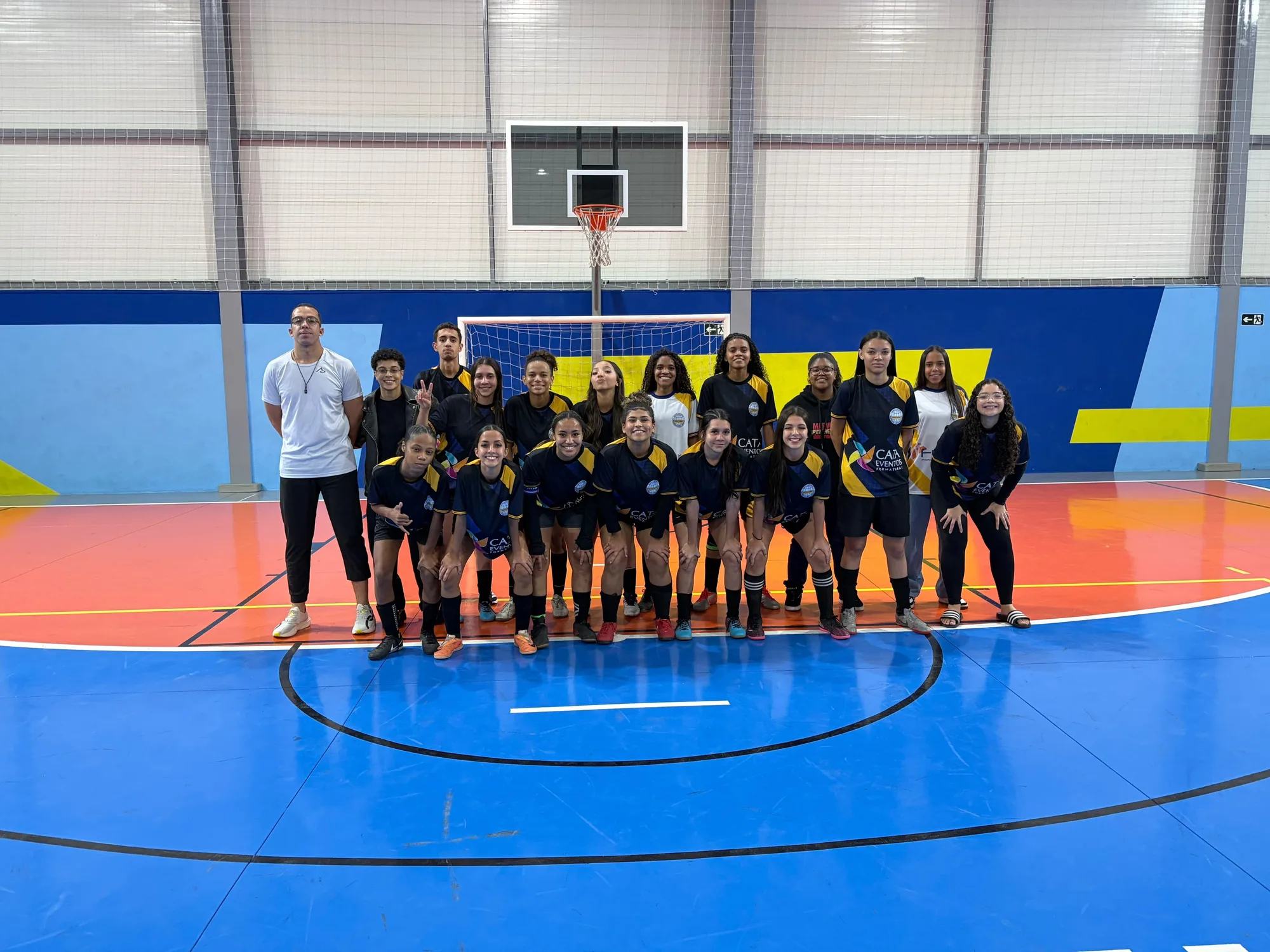 Elenco completo do Futsal feminino e a comissão técnica na quadra coberta, diante do gol